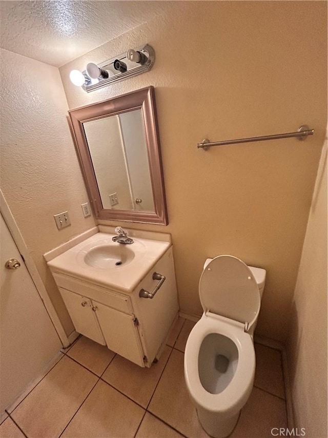 half bath with a textured ceiling, toilet, vanity, and tile patterned flooring