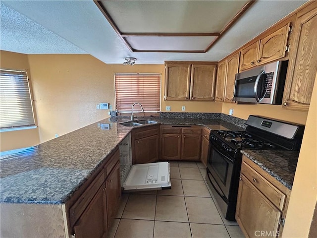 kitchen with a sink, stainless steel microwave, a peninsula, light tile patterned flooring, and black range with gas stovetop