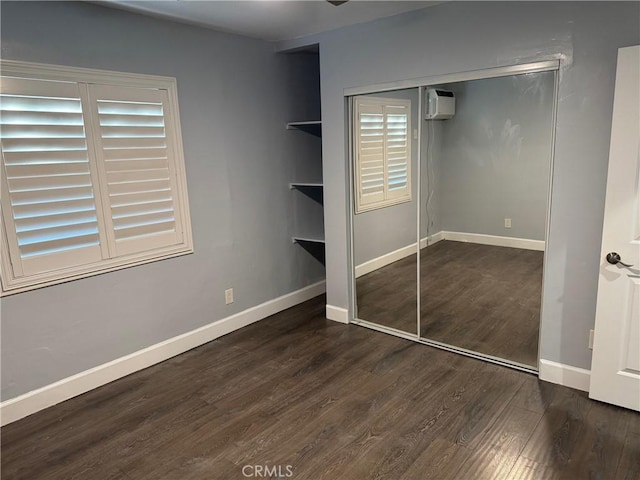 unfurnished bedroom with an AC wall unit, wood finished floors, a closet, and baseboards