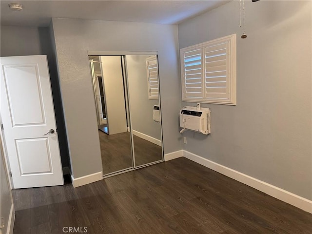 unfurnished bedroom featuring dark wood-style floors, a closet, a wall mounted AC, and baseboards