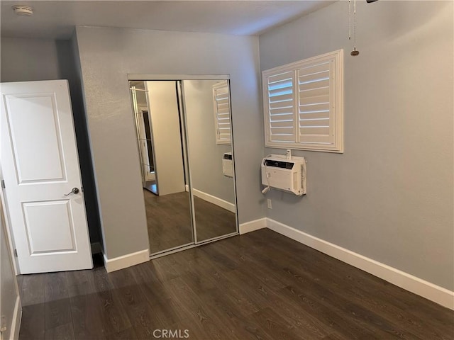 unfurnished bedroom with dark wood-style floors, baseboards, a closet, and a wall mounted AC