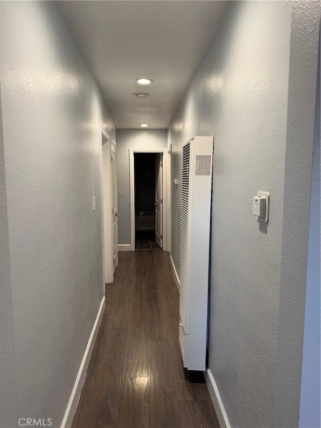 hall featuring dark wood-type flooring, baseboards, and a heating unit