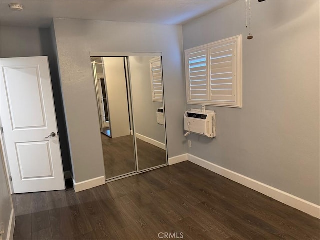 unfurnished bedroom featuring dark wood-type flooring, baseboards, a closet, and a wall mounted AC