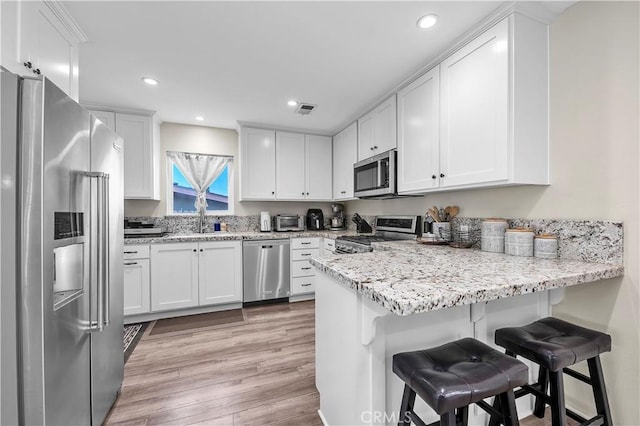 kitchen featuring visible vents, stainless steel appliances, a peninsula, white cabinets, and light wood finished floors