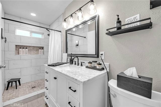 full bath with vanity, toilet, a textured wall, and a tile shower