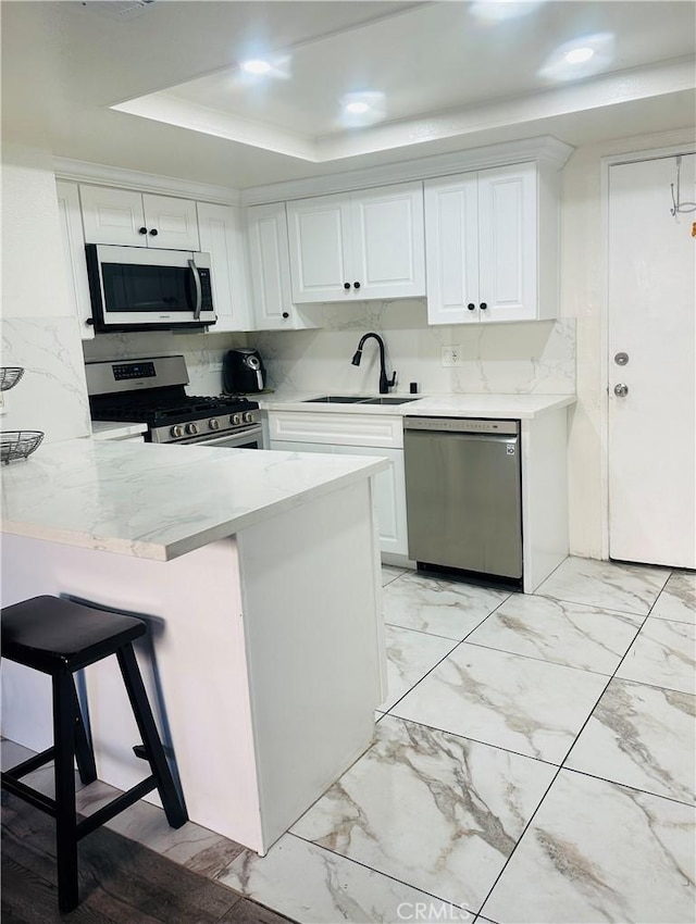 kitchen with marble finish floor, a sink, appliances with stainless steel finishes, a breakfast bar area, and white cabinets