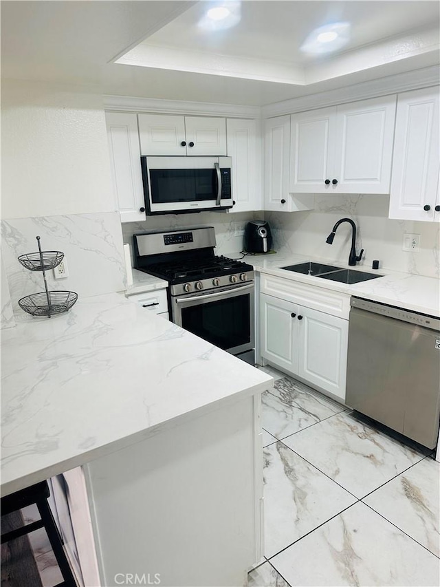 kitchen featuring stainless steel appliances, marble finish floor, white cabinetry, a raised ceiling, and a sink