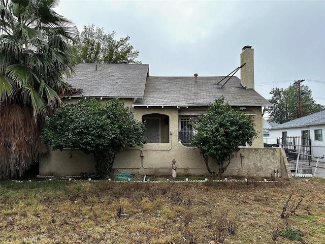 view of front of home with stucco siding, a chimney, and fence