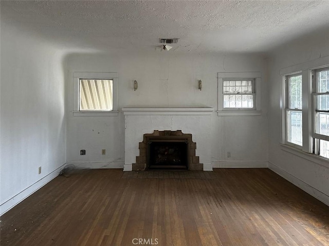 unfurnished living room featuring visible vents, baseboards, a fireplace, hardwood / wood-style flooring, and a textured ceiling