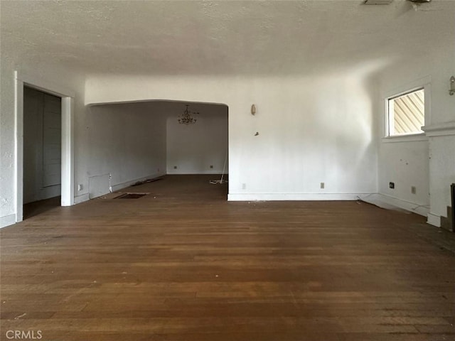 empty room with arched walkways, a notable chandelier, a textured ceiling, and wood finished floors