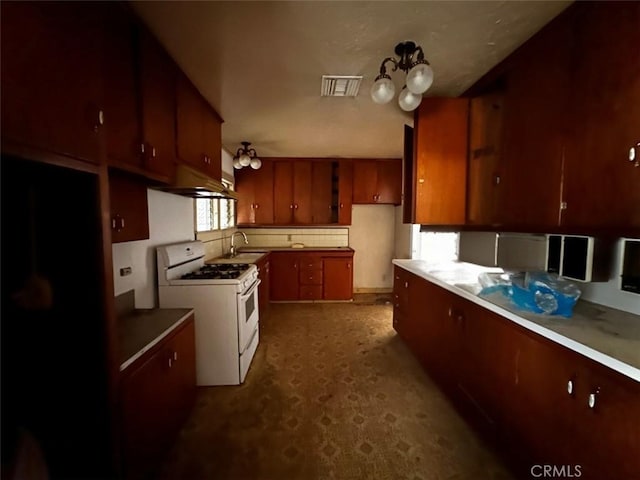 kitchen featuring visible vents, gas range gas stove, a sink, under cabinet range hood, and backsplash