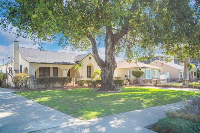 view of front facade featuring stucco siding, a chimney, a front lawn, and fence