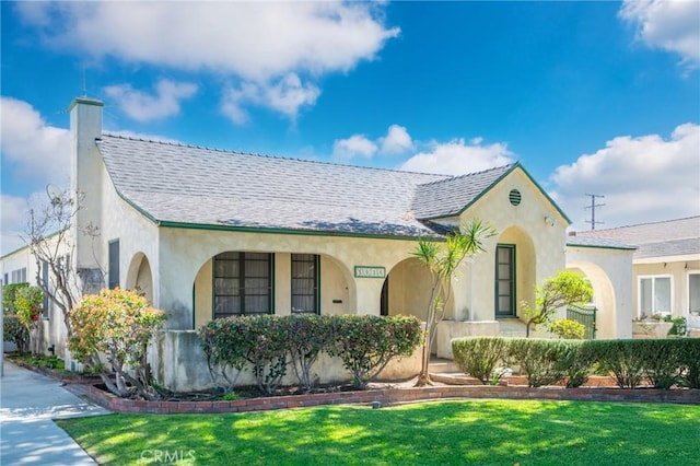 mediterranean / spanish-style house with a chimney, stucco siding, a shingled roof, and a front yard