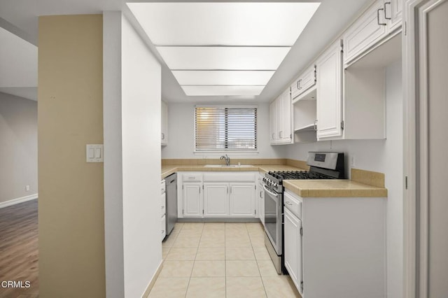 kitchen featuring light tile patterned floors, a sink, light countertops, appliances with stainless steel finishes, and white cabinetry