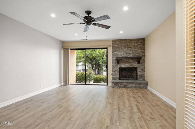 unfurnished living room with visible vents, wood finished floors, a stone fireplace, baseboards, and ceiling fan