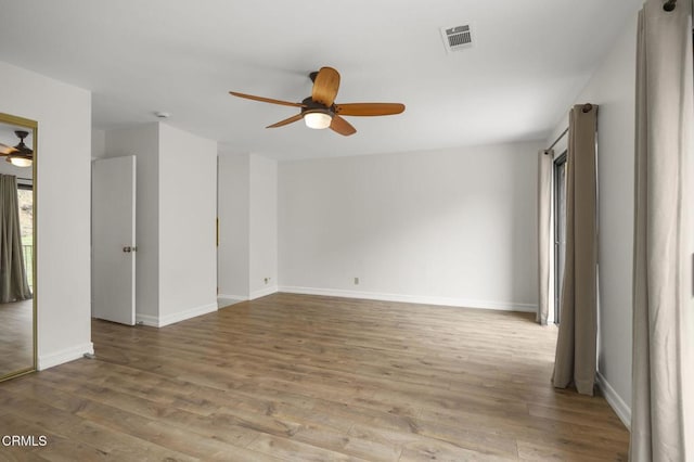 empty room with a ceiling fan, wood finished floors, visible vents, and baseboards