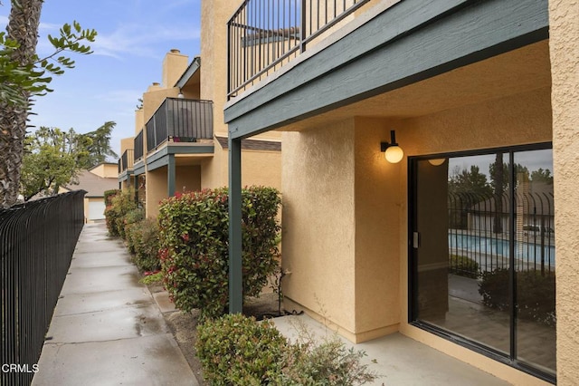 view of home's exterior with stucco siding, a balcony, and fence