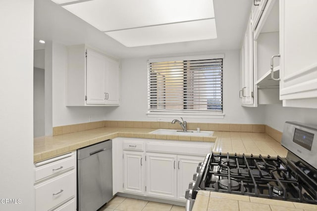 kitchen with a sink, tile countertops, white cabinetry, and stainless steel appliances