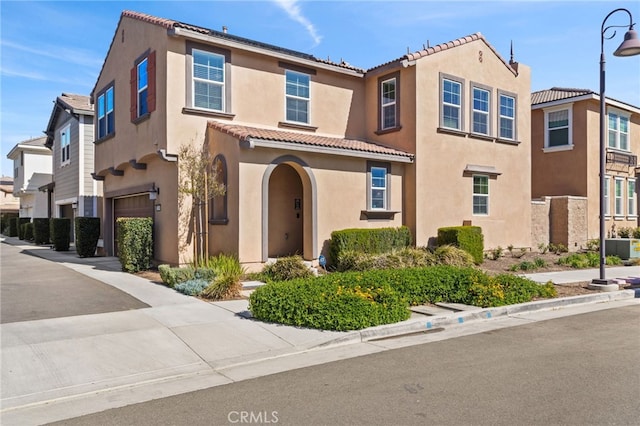 view of front of house with a residential view, stucco siding, a tiled roof, and a garage