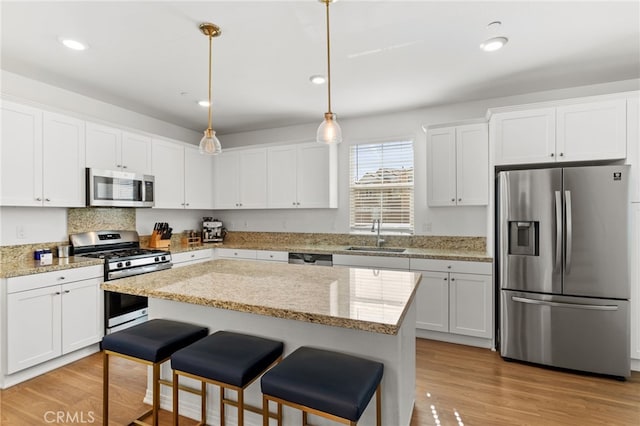 kitchen featuring a breakfast bar area, light wood-style flooring, a sink, stainless steel appliances, and white cabinetry