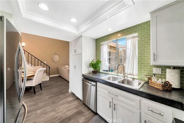 kitchen with a sink, a raised ceiling, appliances with stainless steel finishes, and crown molding