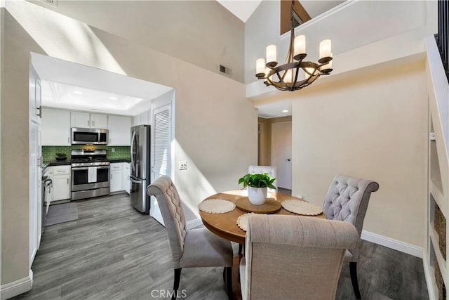 dining room featuring visible vents, dark wood-type flooring, baseboards, a tray ceiling, and an inviting chandelier