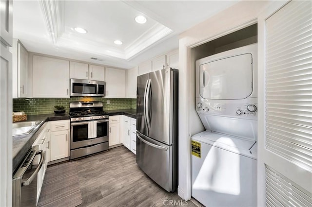 kitchen featuring decorative backsplash, a tray ceiling, stacked washer / drying machine, and stainless steel appliances