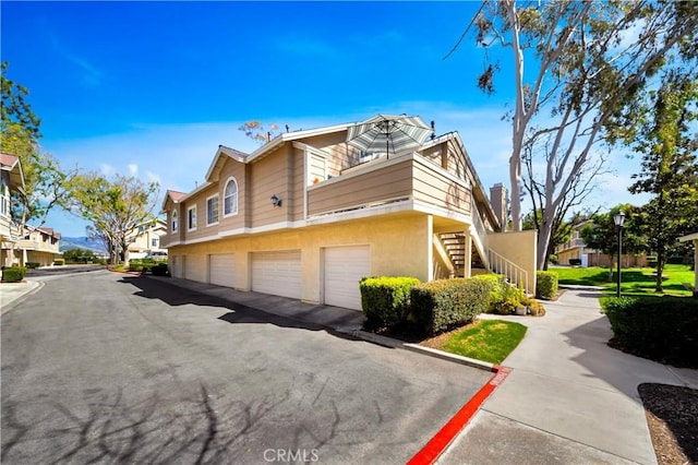 view of property exterior featuring community garages, stairway, a residential view, and stucco siding