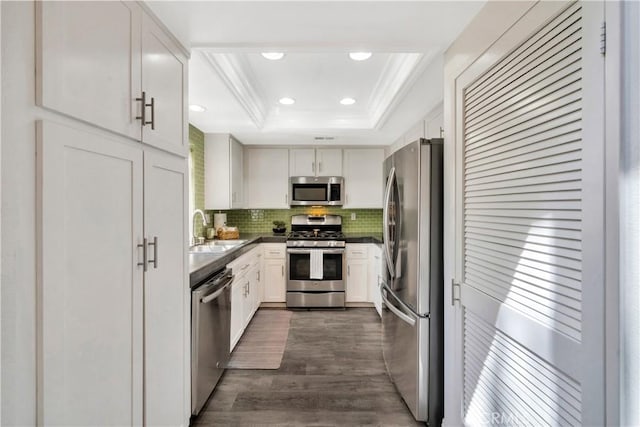 kitchen with a sink, dark countertops, stainless steel appliances, crown molding, and a raised ceiling