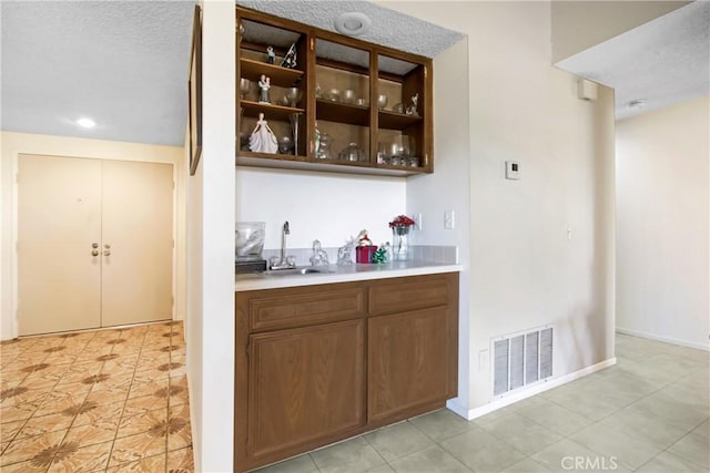 bar with visible vents, a textured ceiling, baseboards, and a sink