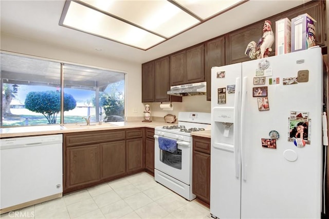 kitchen featuring white appliances, light countertops, under cabinet range hood, and a sink