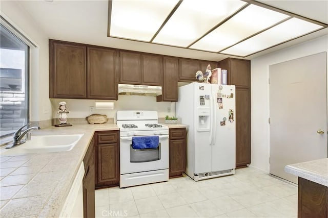 kitchen featuring white appliances, tile countertops, a sink, dark brown cabinetry, and under cabinet range hood