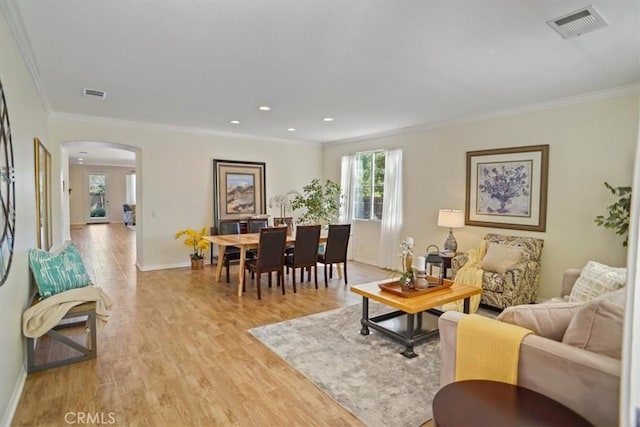 living area featuring arched walkways, visible vents, crown molding, and light wood-type flooring