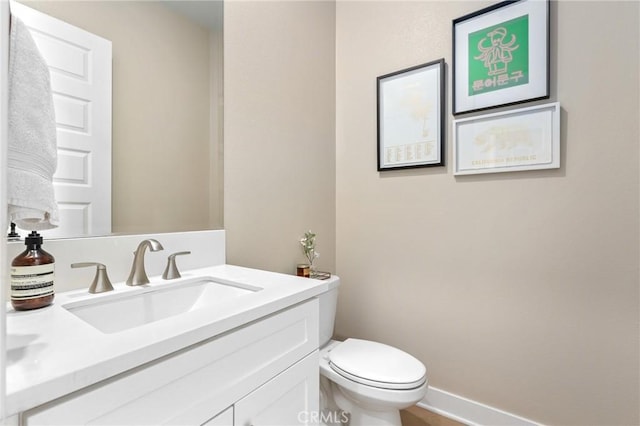 half bath featuring baseboards, toilet, and vanity