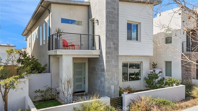 view of front of house with a balcony, fence, and stucco siding