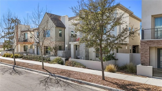 view of front of house with a balcony, fence, stone siding, and stucco siding