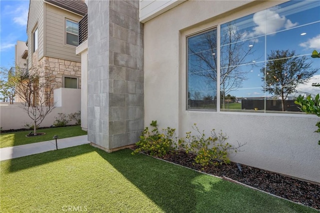 view of side of property featuring a yard, stone siding, stucco siding, and fence