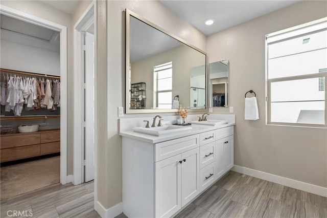 bathroom featuring double vanity, a spacious closet, baseboards, and a sink