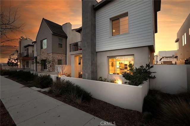 contemporary home featuring a fenced front yard, stone siding, stucco siding, and a balcony