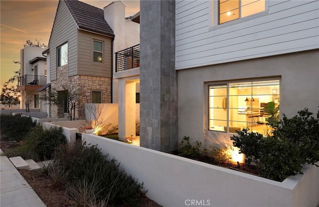 property exterior at dusk with a fenced front yard, stone siding, and a balcony