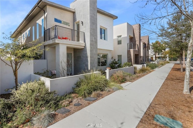 view of side of property with a balcony, fence, and stucco siding