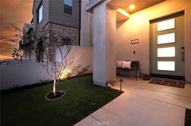 property entrance featuring a patio area, stone siding, stucco siding, and a yard