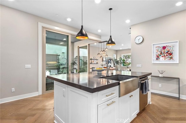 kitchen featuring a kitchen island with sink, a sink, dark countertops, recessed lighting, and white cabinets