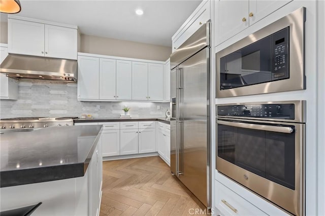 kitchen featuring under cabinet range hood, built in appliances, backsplash, and white cabinets