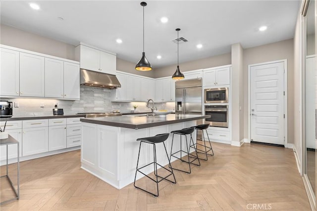 kitchen with visible vents, built in appliances, under cabinet range hood, dark countertops, and tasteful backsplash