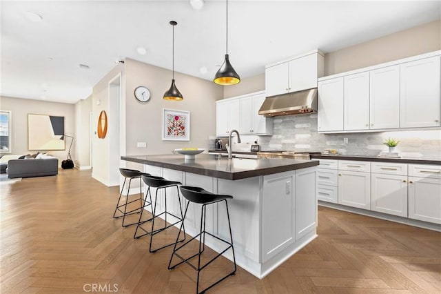 kitchen featuring dark countertops, backsplash, under cabinet range hood, a breakfast bar area, and a sink