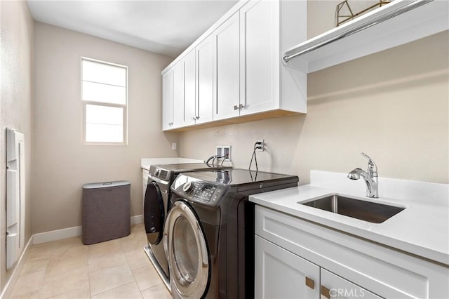 laundry room with baseboards, light tile patterned floors, separate washer and dryer, cabinet space, and a sink