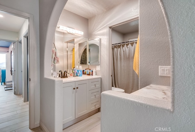 bathroom with vanity, wood finished floors, a shower with curtain, and a textured wall