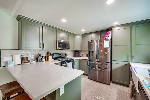 kitchen with stainless steel appliances, a peninsula, green cabinets, and light countertops