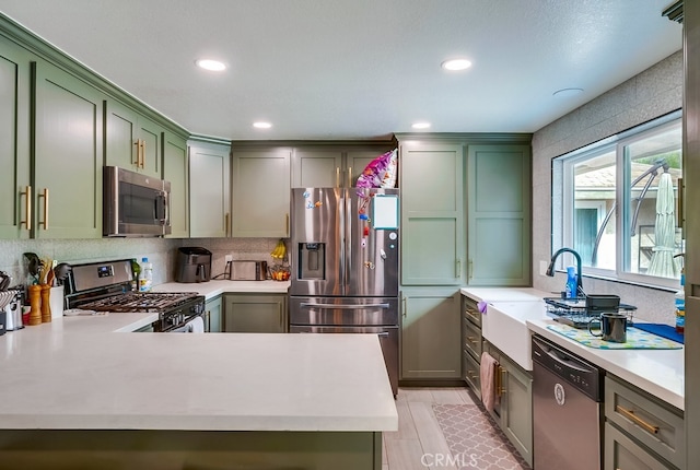 kitchen with a sink, decorative backsplash, light countertops, stainless steel appliances, and green cabinets